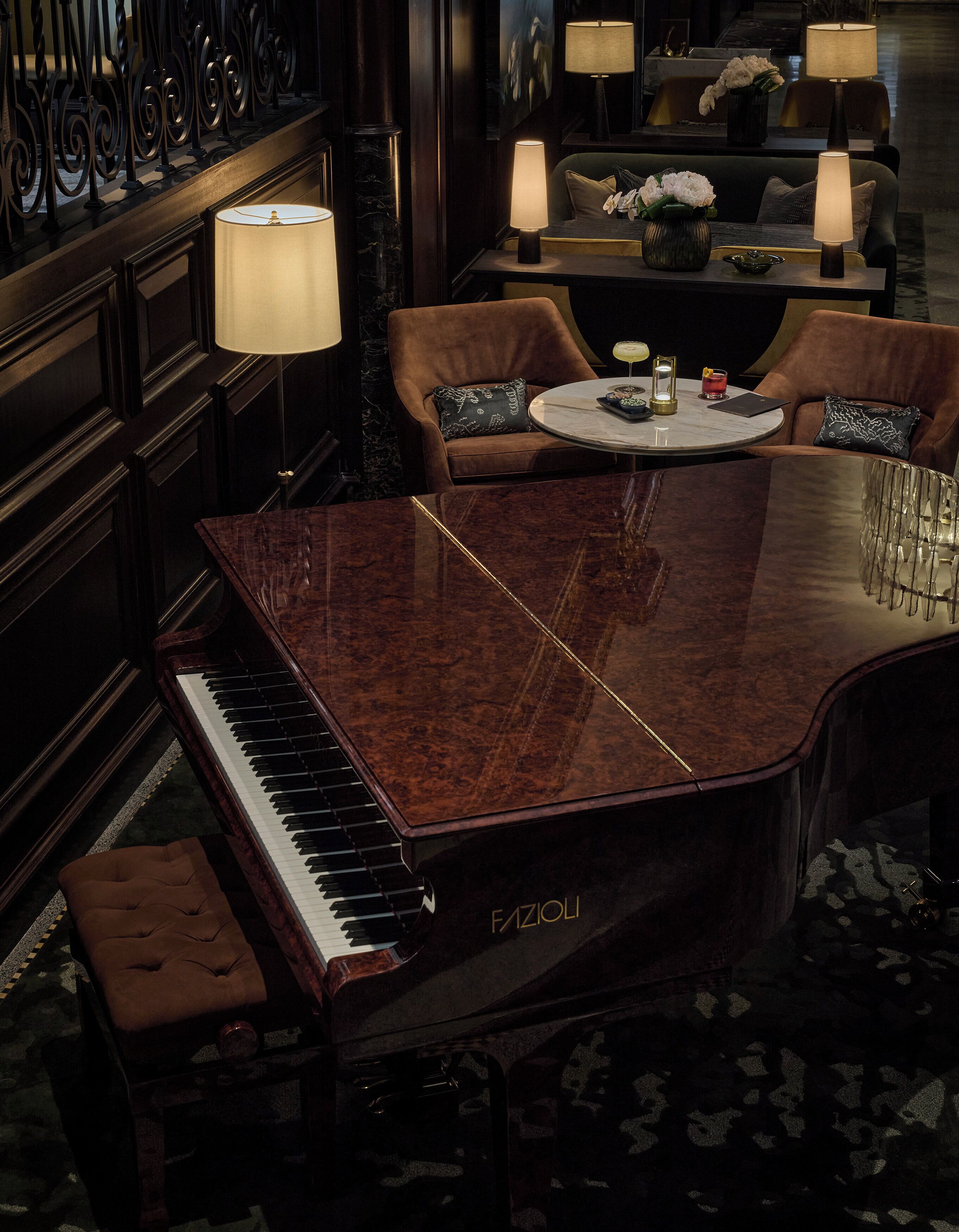 A grand piano, a round table with a vase of flowers, and a sofa with cushions in a luxurious room.