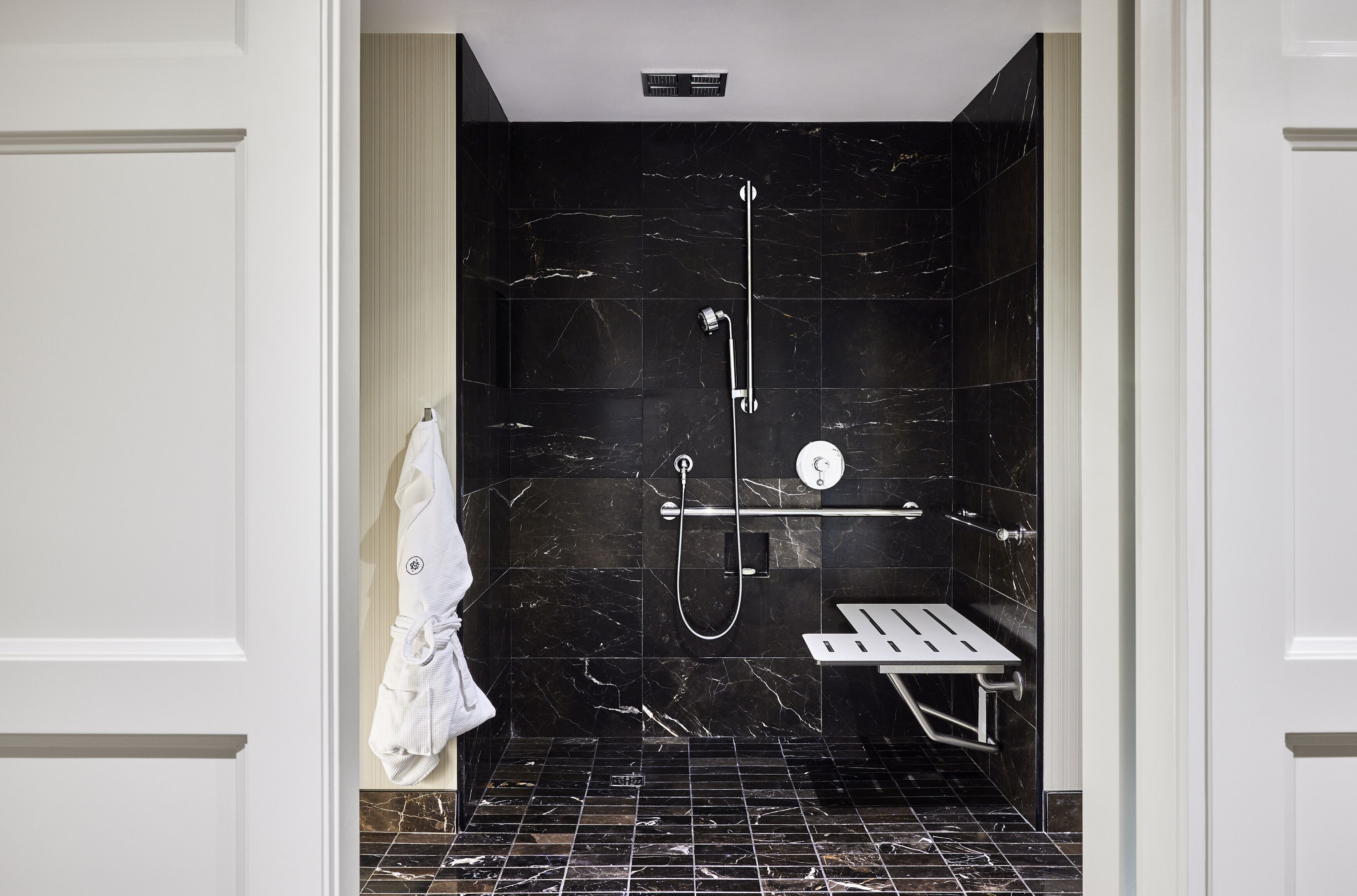 A modern bathroom with a black marble shower, a white towel rack, and a small bench.