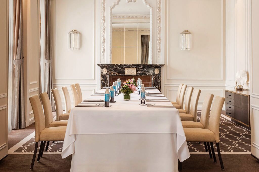 Une salle à manger élégante, avec une longue table, des chaises, une cheminée et des appliques murales.