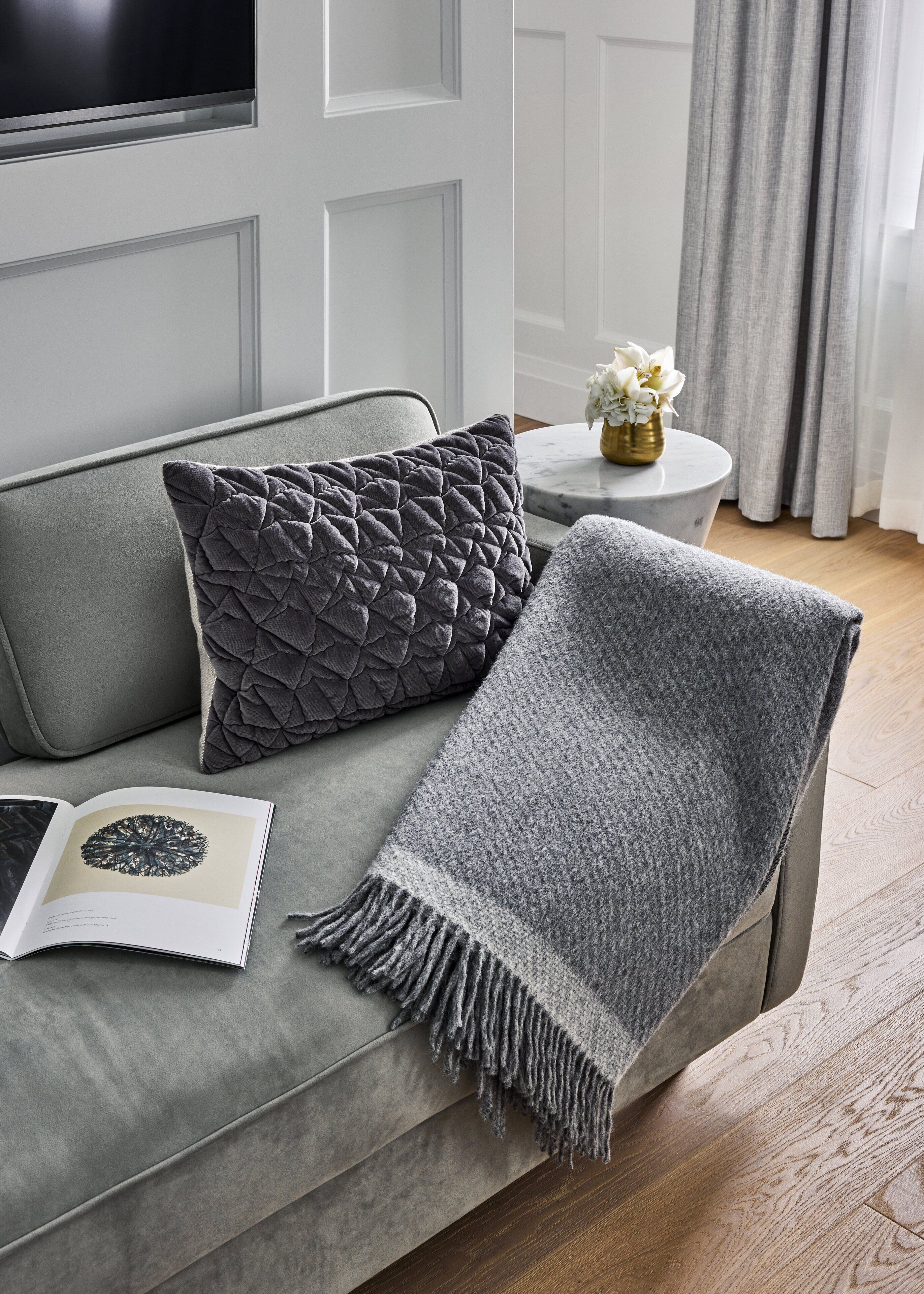 Un sofá gris con una manta gris y un cojín decorativo.