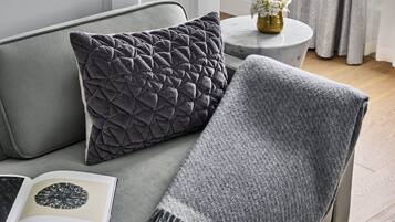 Un sofá gris con una manta gris y un cojín decorativo.