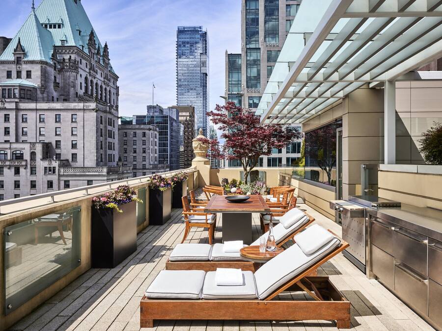 A rooftop terrace with a dining area, lounge chairs, and a view of city buildings.