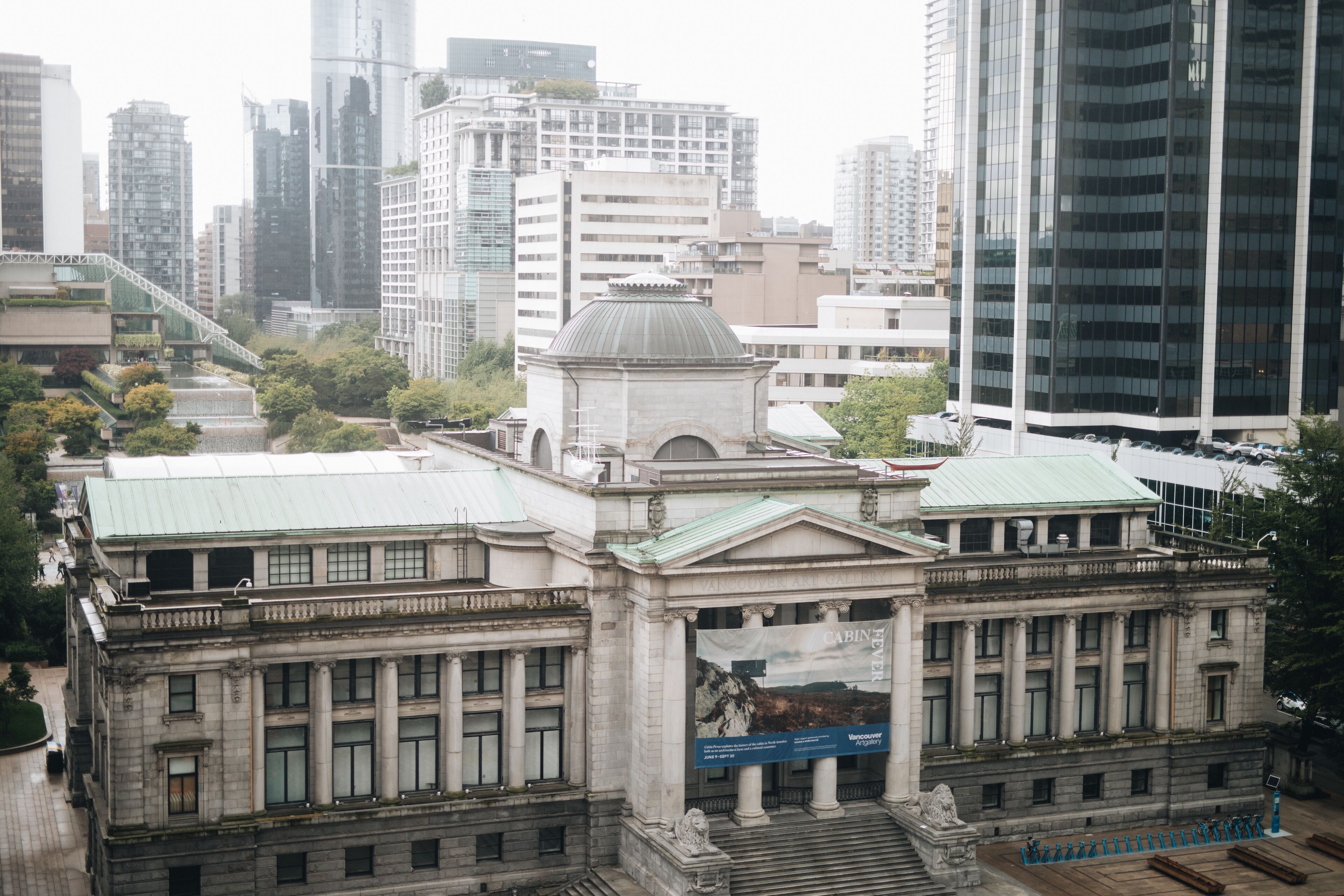 Un bâtiment historique à l’architecture classique, avec des colonnes et un dôme, entouré d’immeubles modernes de grande hauteur.