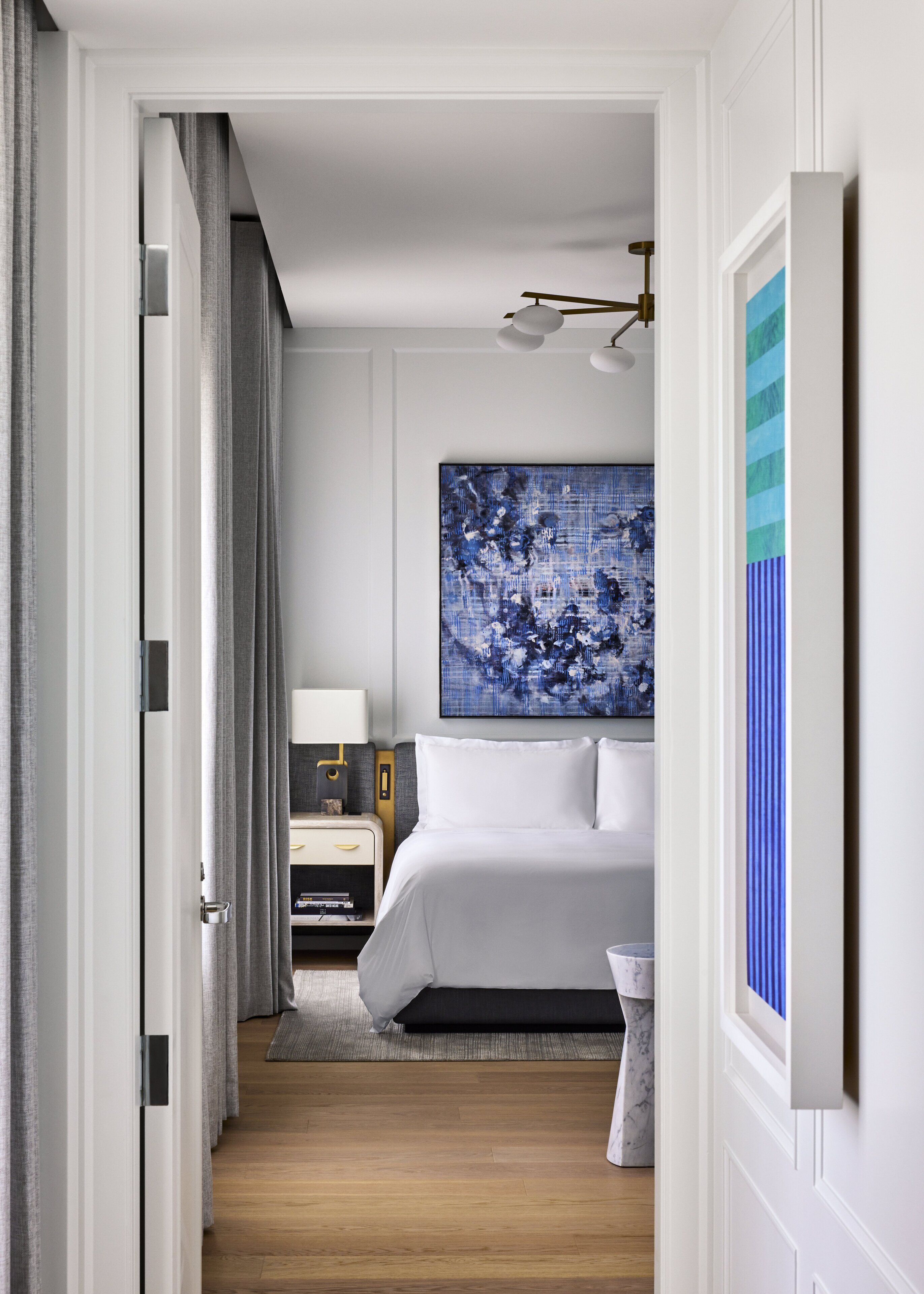 Habitación de hotel con cama, mesita de noche, lámpara y un cuadro abstracto grande en la pared.