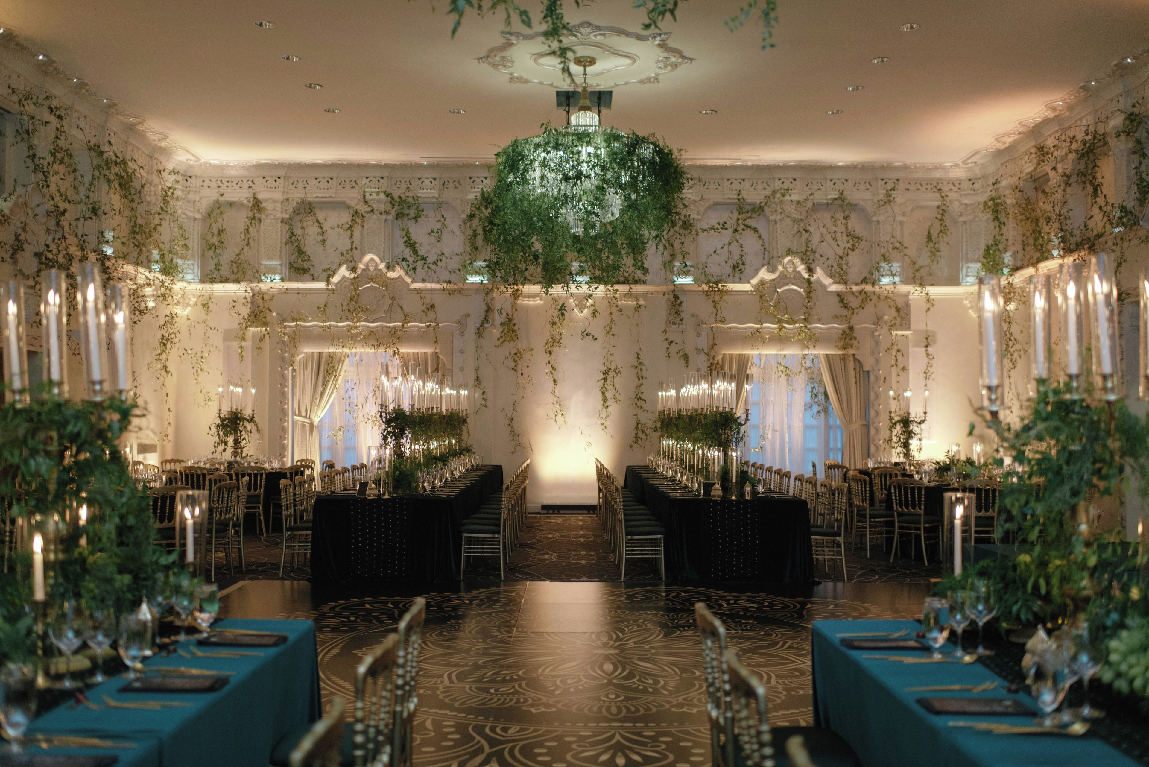 Un salón imponente con candelabro, techo ornamentado y filas de mesas con sillas.
