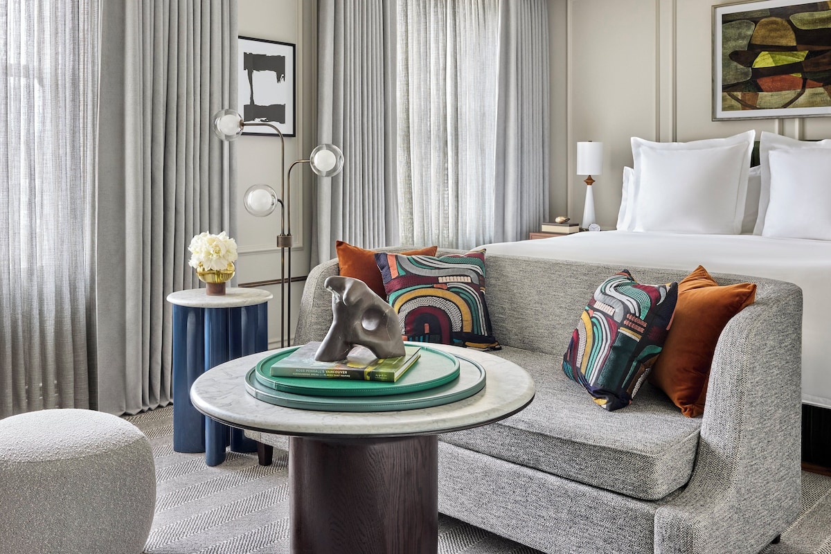 Habitación de hotel con cama, sofá, una mesa redonda con una escultura, lámpara y un cuadro en la pared.