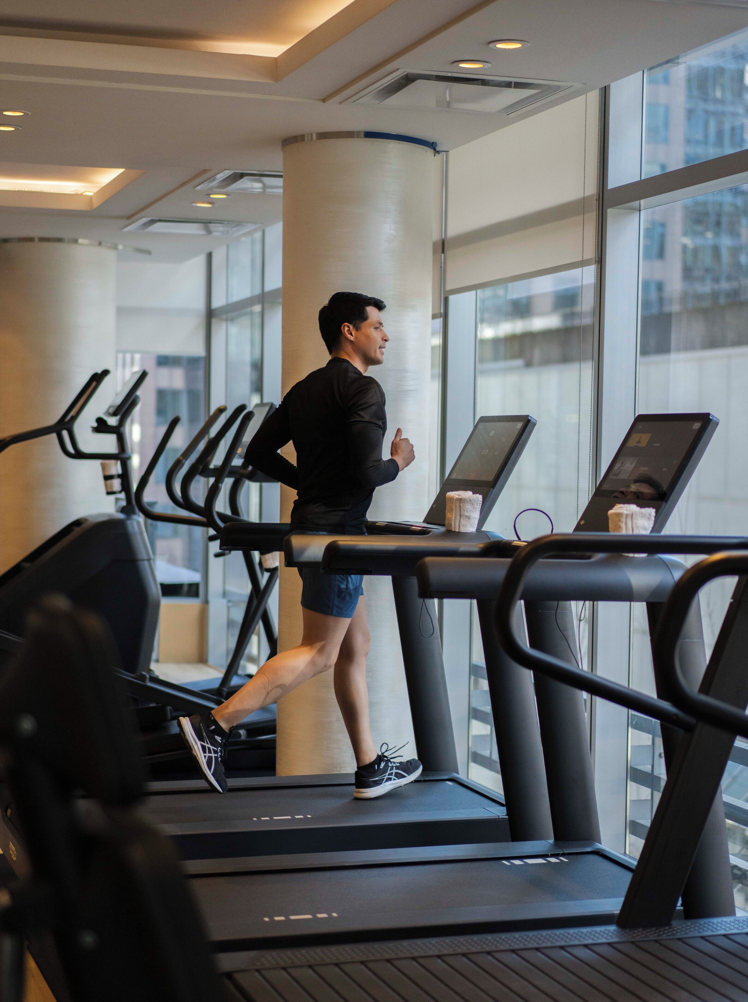 A person running on a treadmill in a modern gym with large windows and a minimalist design.
