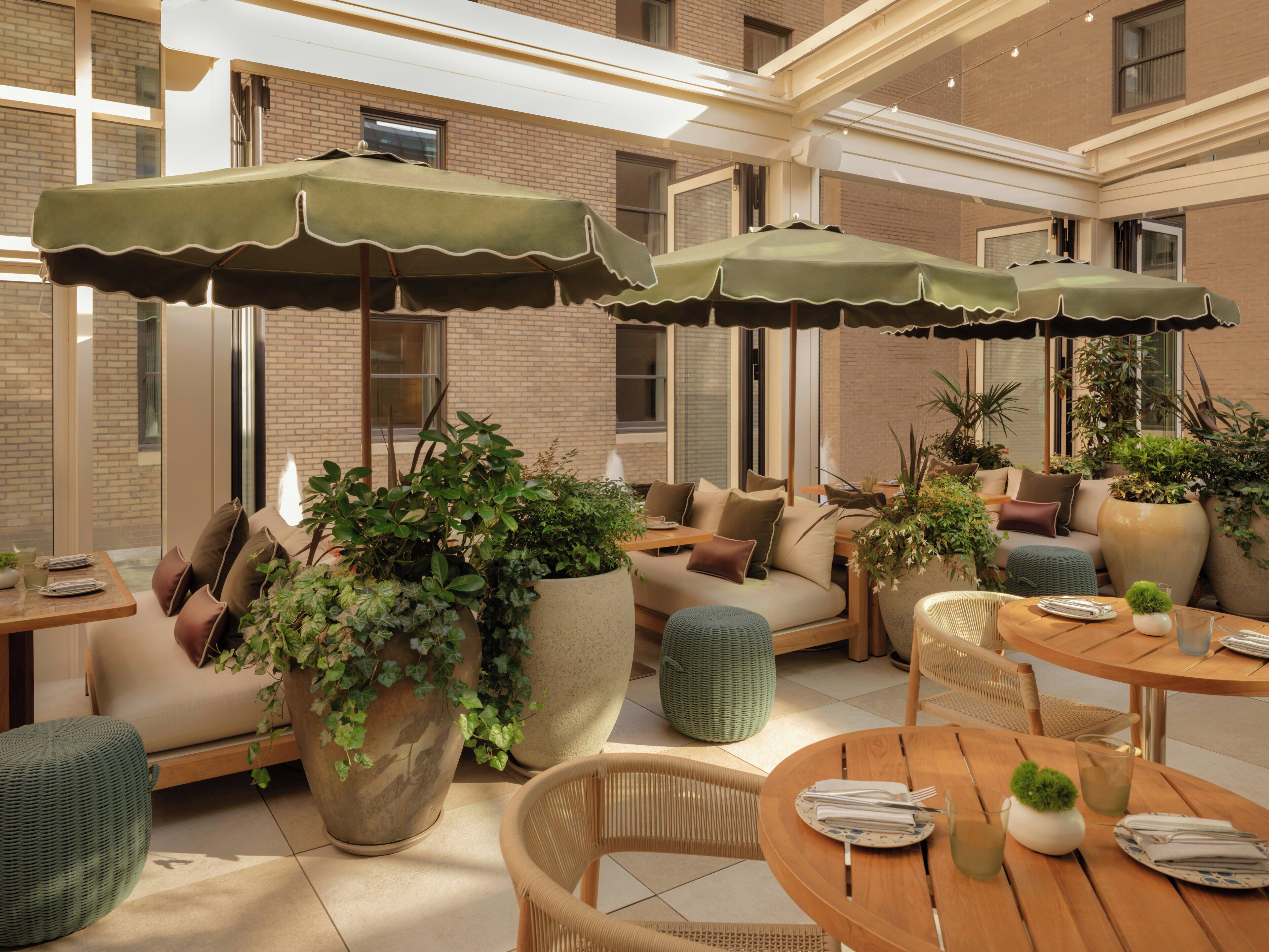 A well-lit outdoor seating area with multiple tables and chairs, surrounded by large potted plants and umbrellas.