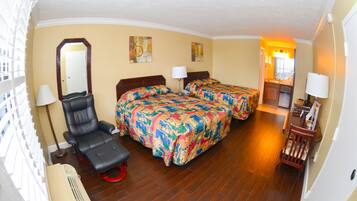 A hotel room with two beds, a chair, a desk, a mirror, and a small kitchenette.