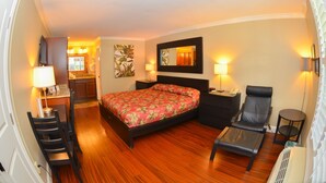 A hotel room with a bed, a desk with a chair, a small table, a chair, and a nightstand. - Gulfcoast Inn Naples (Naples)