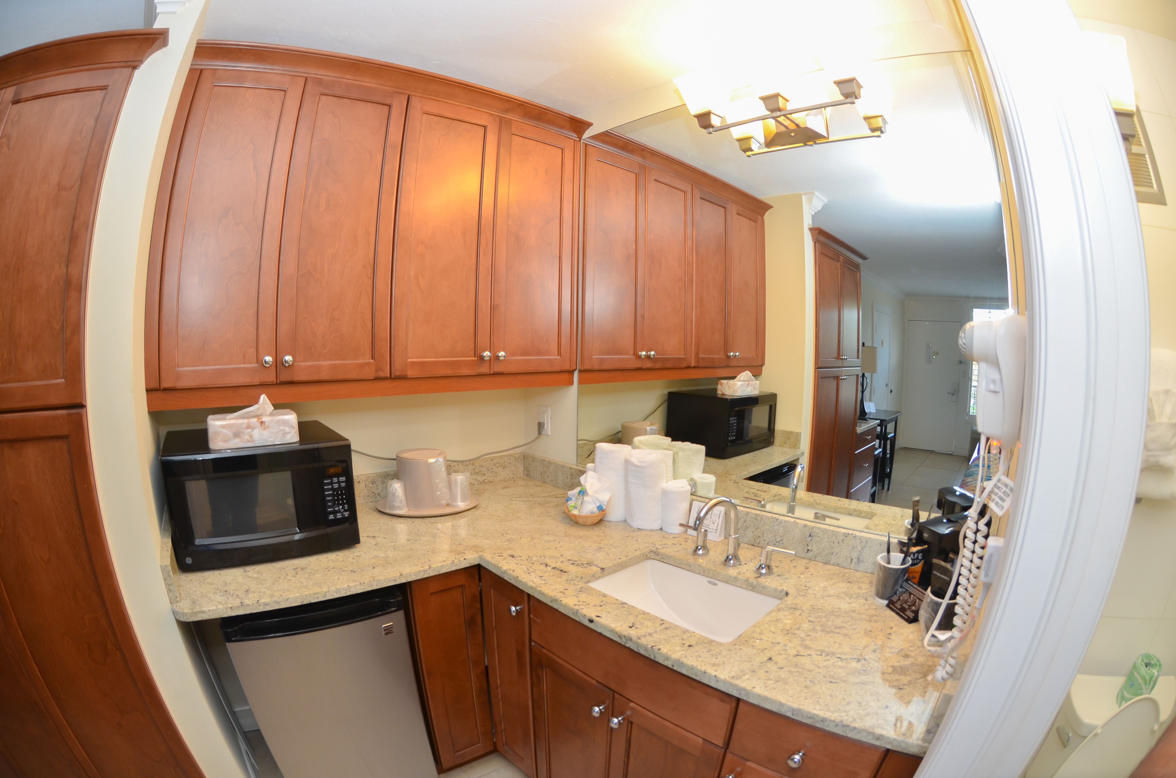 A kitchen with wooden cabinets, a microwave, a sink, and a countertop with various items.