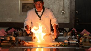 A chef performing a flambé with a flaming pan on a table. - Gulfcoast Inn Naples (Naples)