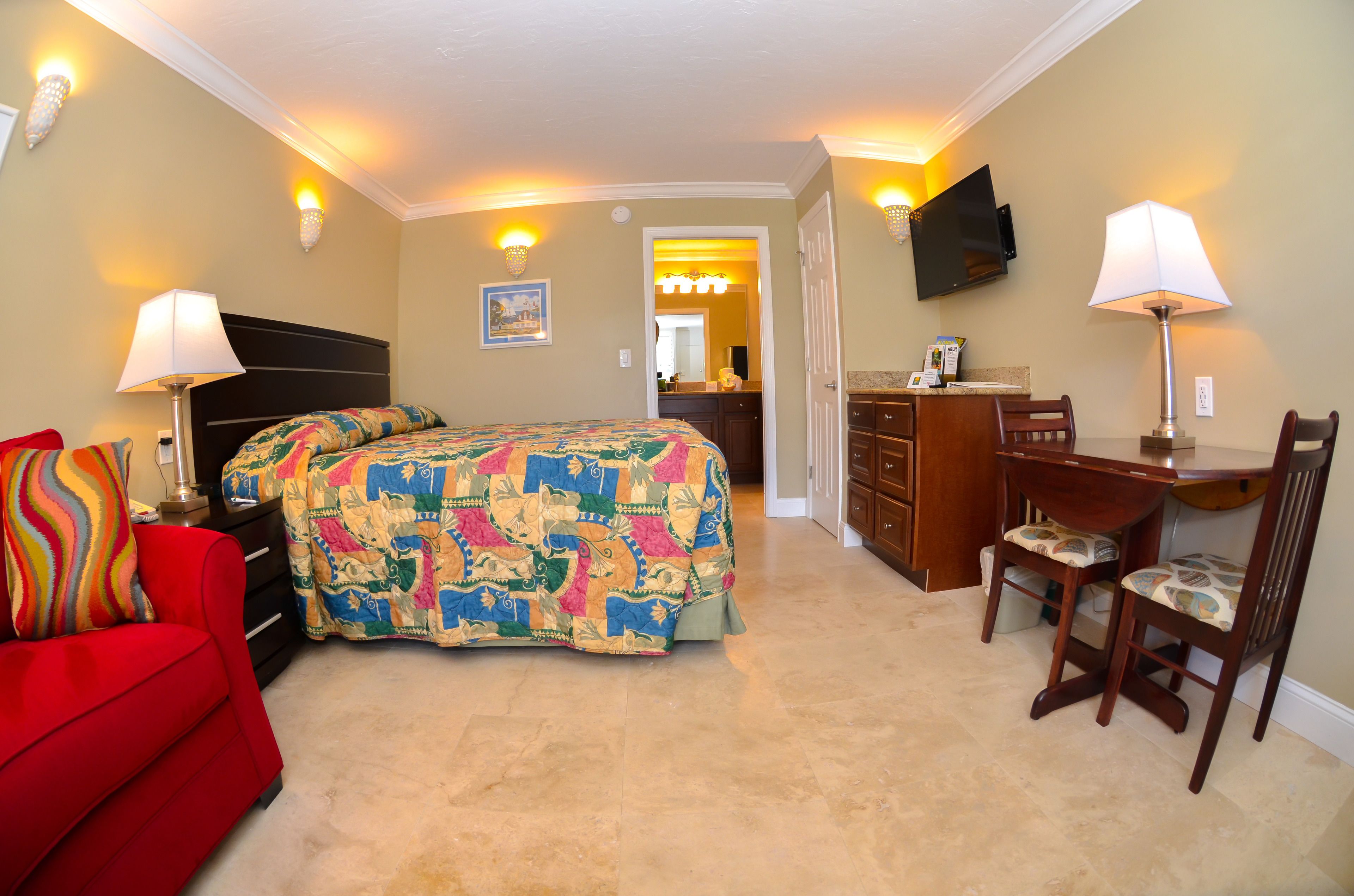 A hotel room with a bed, a desk, a chair, a TV, and a red sofa.
