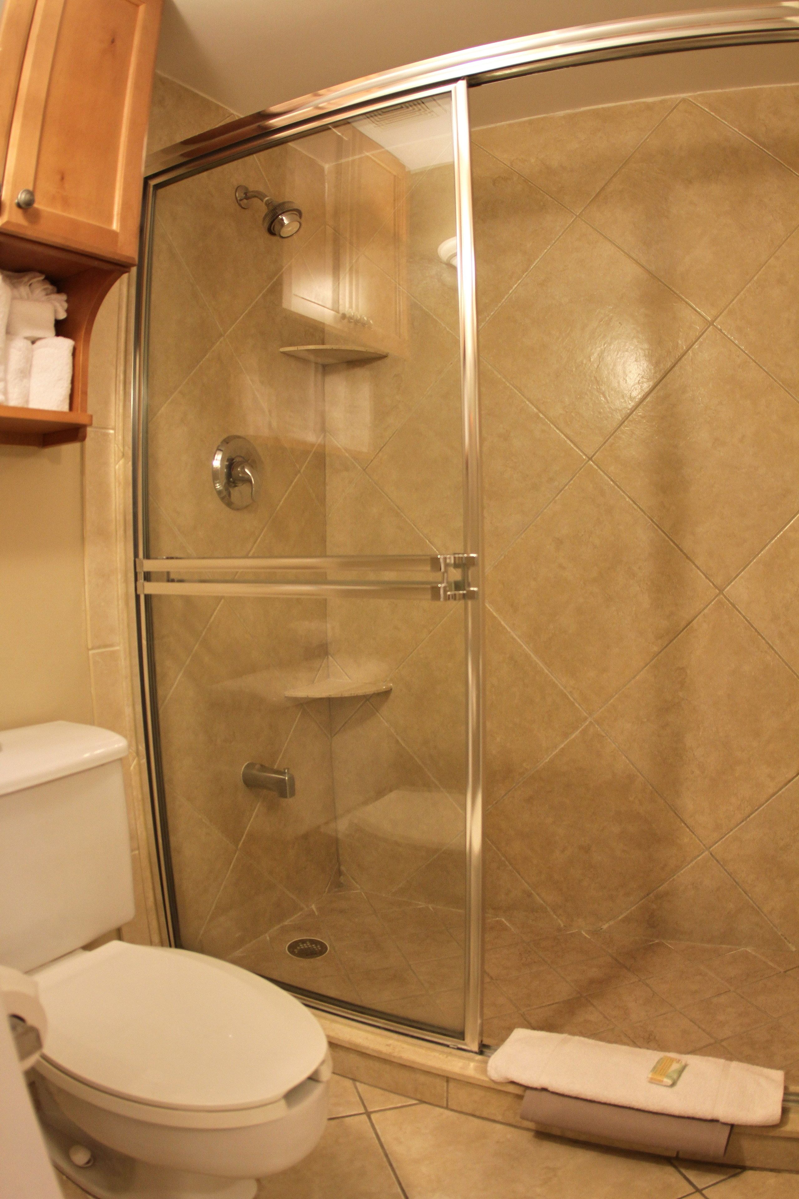 Un baño con ducha de vidrio, un inodoro y un mueble de madera sobre el inodoro.