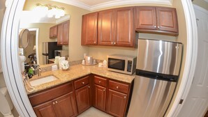 A kitchen with wooden cabinets, stainless steel appliances, a granite countertop, and a built-in microwave. - Gulfcoast Inn Naples (Naples)