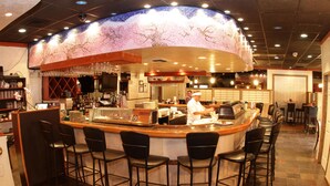 A bar area with a curved counter, bar stools, and a chef preparing food. - Gulfcoast Inn Naples (Naples)