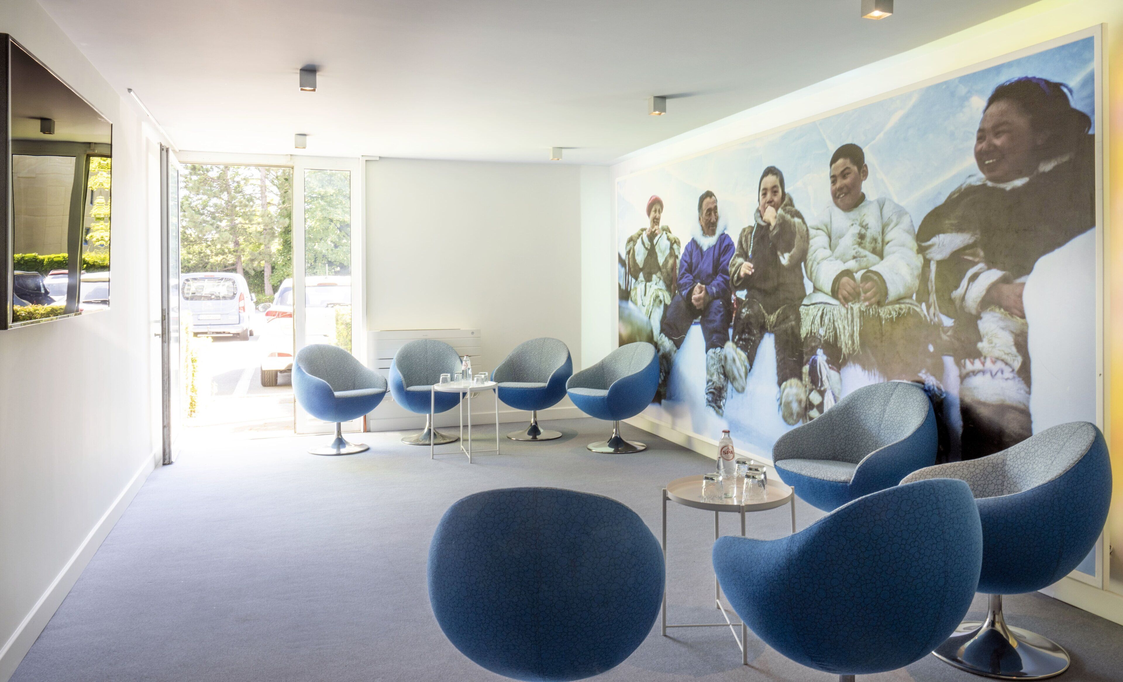 A modern interior with blue chairs, a large wall mural, and a view through a glass door.