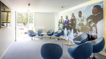 A modern interior with blue chairs, a large wall mural, and a view through a glass door.