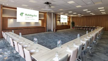 A conference room with a long table, chairs, and a projector screen displaying the Holiday Inn Brussels Airport logo.