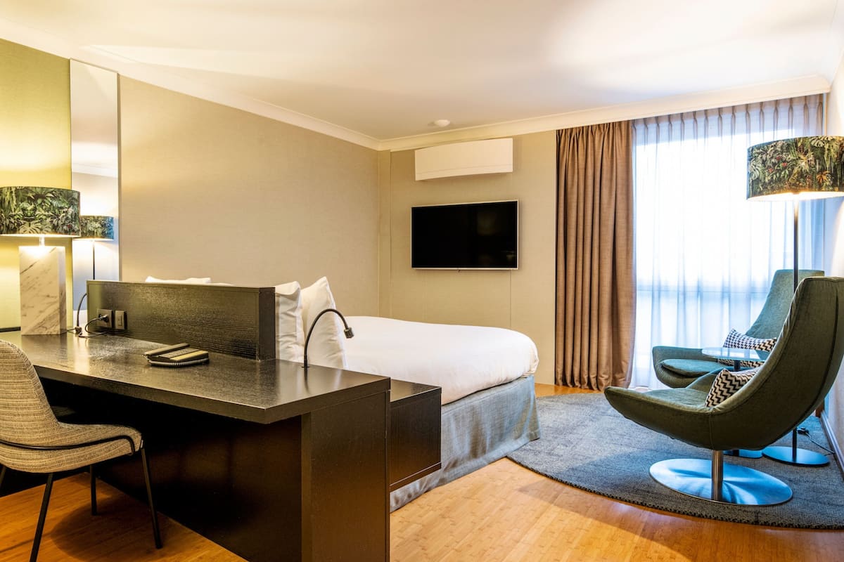 A modern hotel room with a bed, desk, chair, and a flat-screen TV.