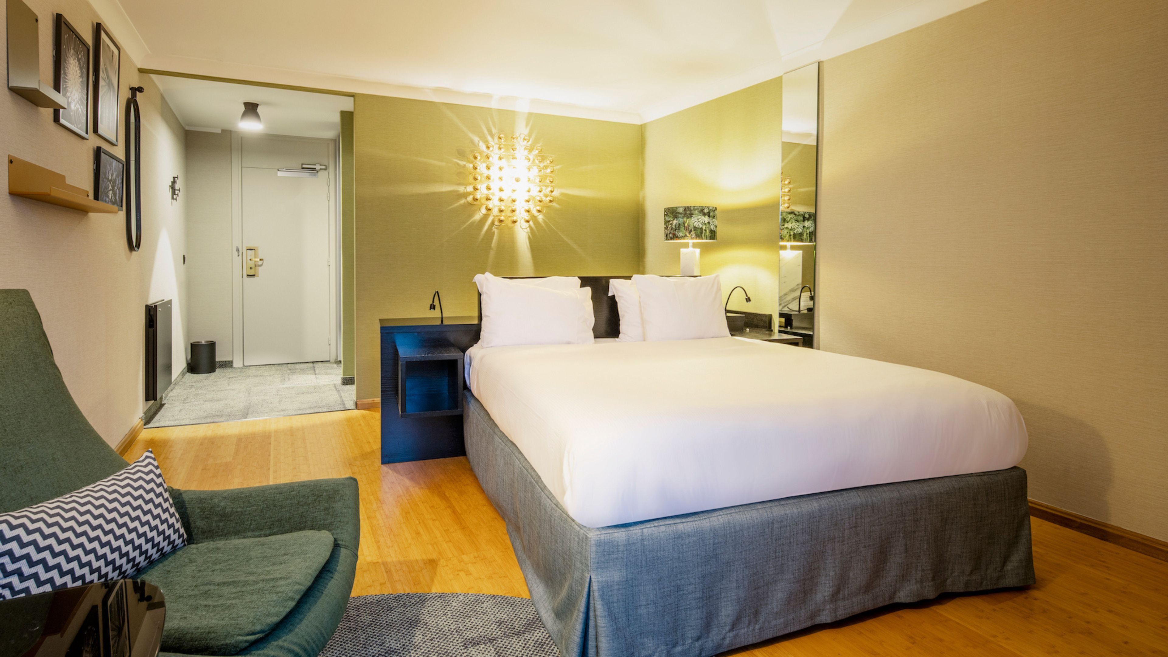 A hotel room with a large bed, a desk, a chair, and a mirror.