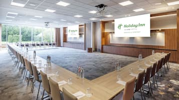 Una sala de conferencias con una mesa larga, sillas y una pantalla mostrando el logotipo de Holiday Inn Brussels Airport.