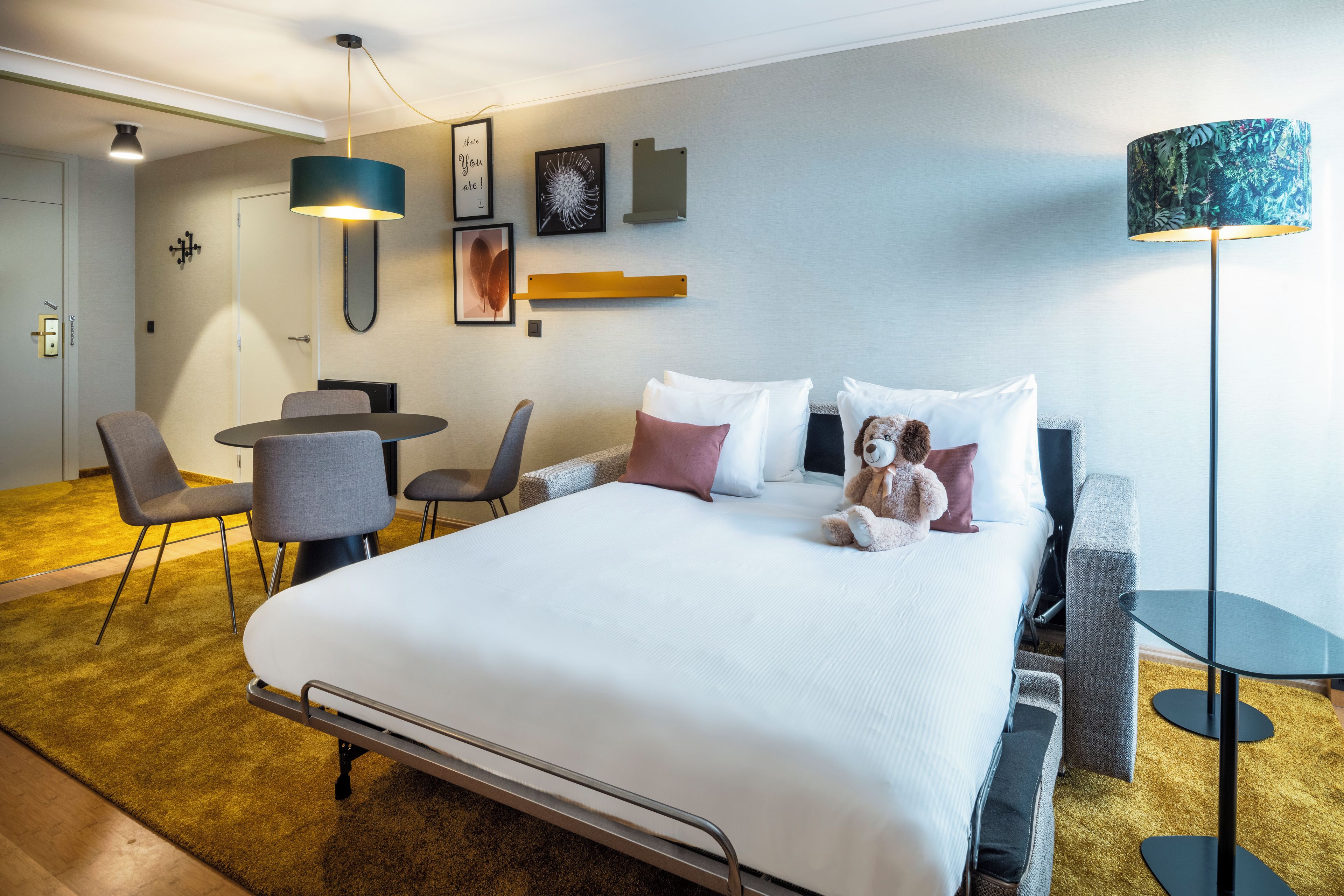 Una habitación de hotel con una cama, mesita de noche, sillas, un escritorio y una lámpara.