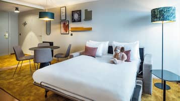 Una habitación de hotel con una cama, mesita de noche, sillas, un escritorio y una lámpara.