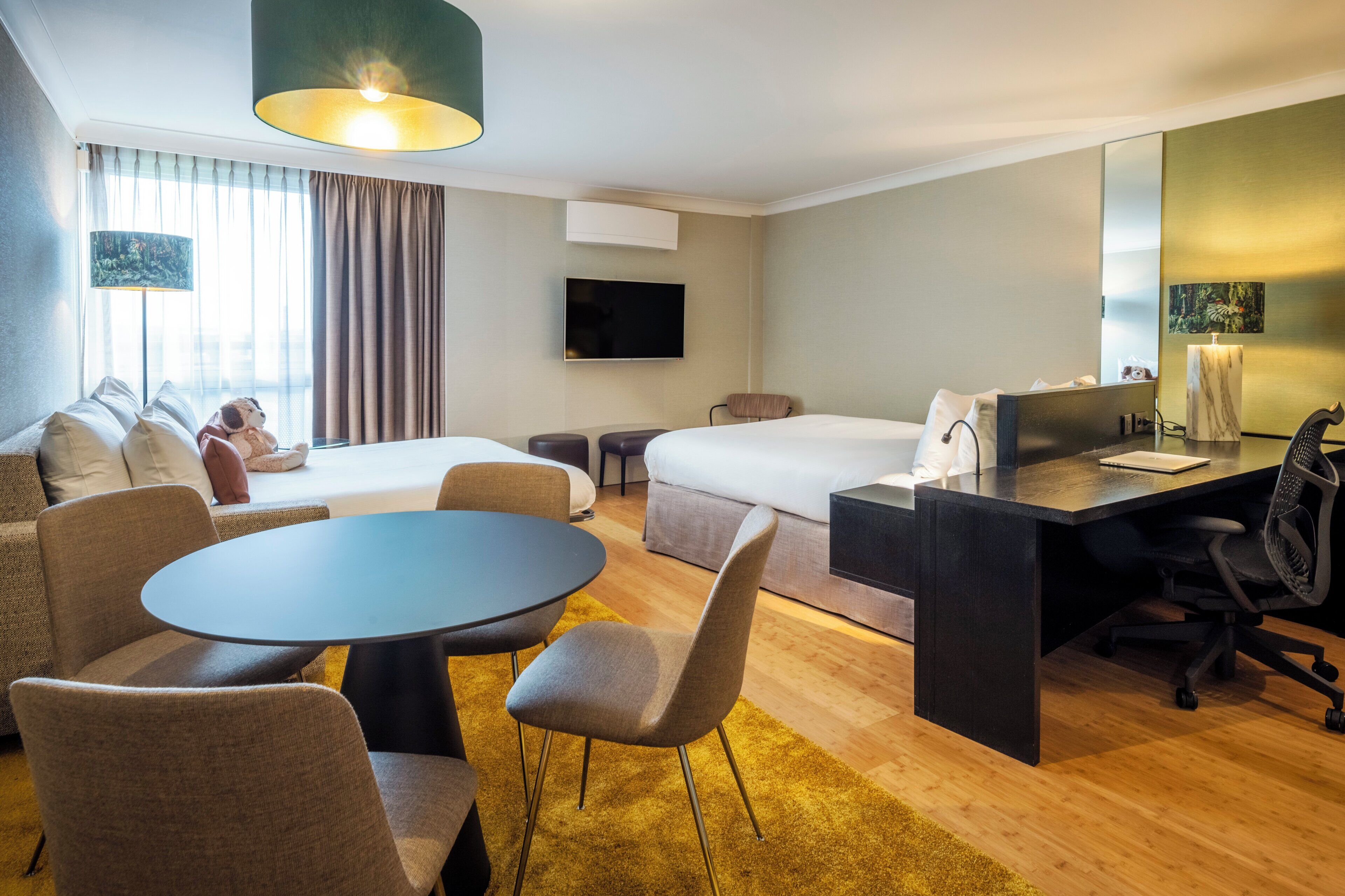 A hotel room with a bed, a desk, a chair, a sofa, a TV, and a window with curtains.