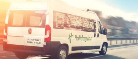 A white Holiday Inn Airport Shuttle driving on a highway.