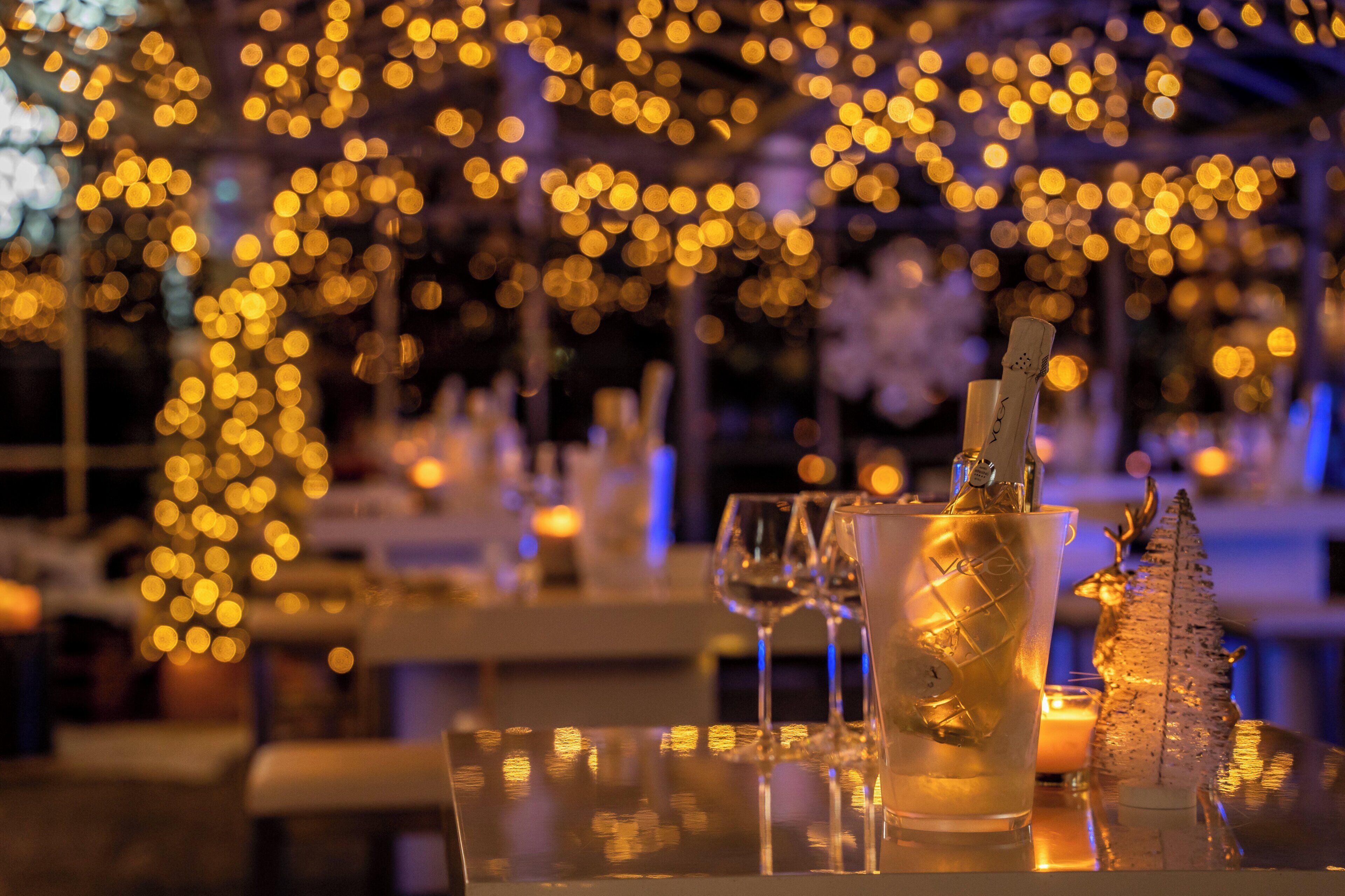 A table set with a champagne bottle, glasses, and a decorative item, surrounded by warm lighting.