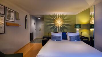 A hotel room with a large bed, bedside tables, a nightstand, a mirror, and a wall-mounted light fixture.