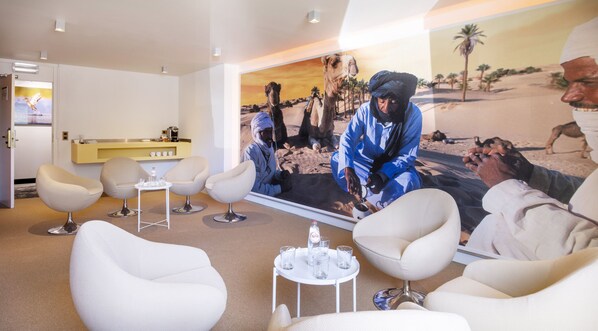 A modern lounge with white chairs, a small table with glasses, and a large desert-themed mural. - Holiday Inn Brussels Airport by IHG (Machelen)