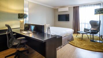 A hotel room with a bed, desk, chair, TV, and a large window with curtains.