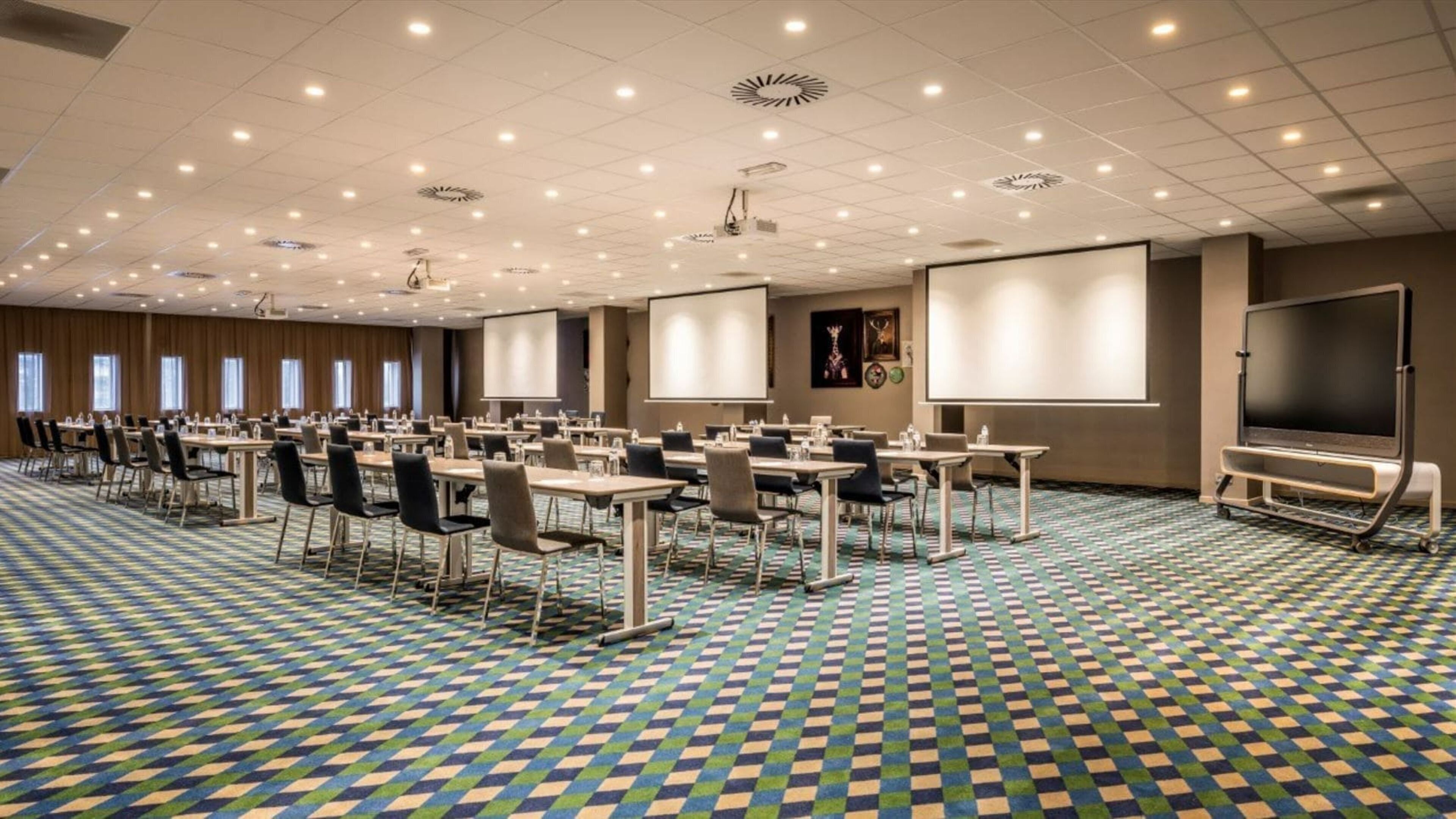 A conference room with multiple tables and chairs, a large screen, and a projector.