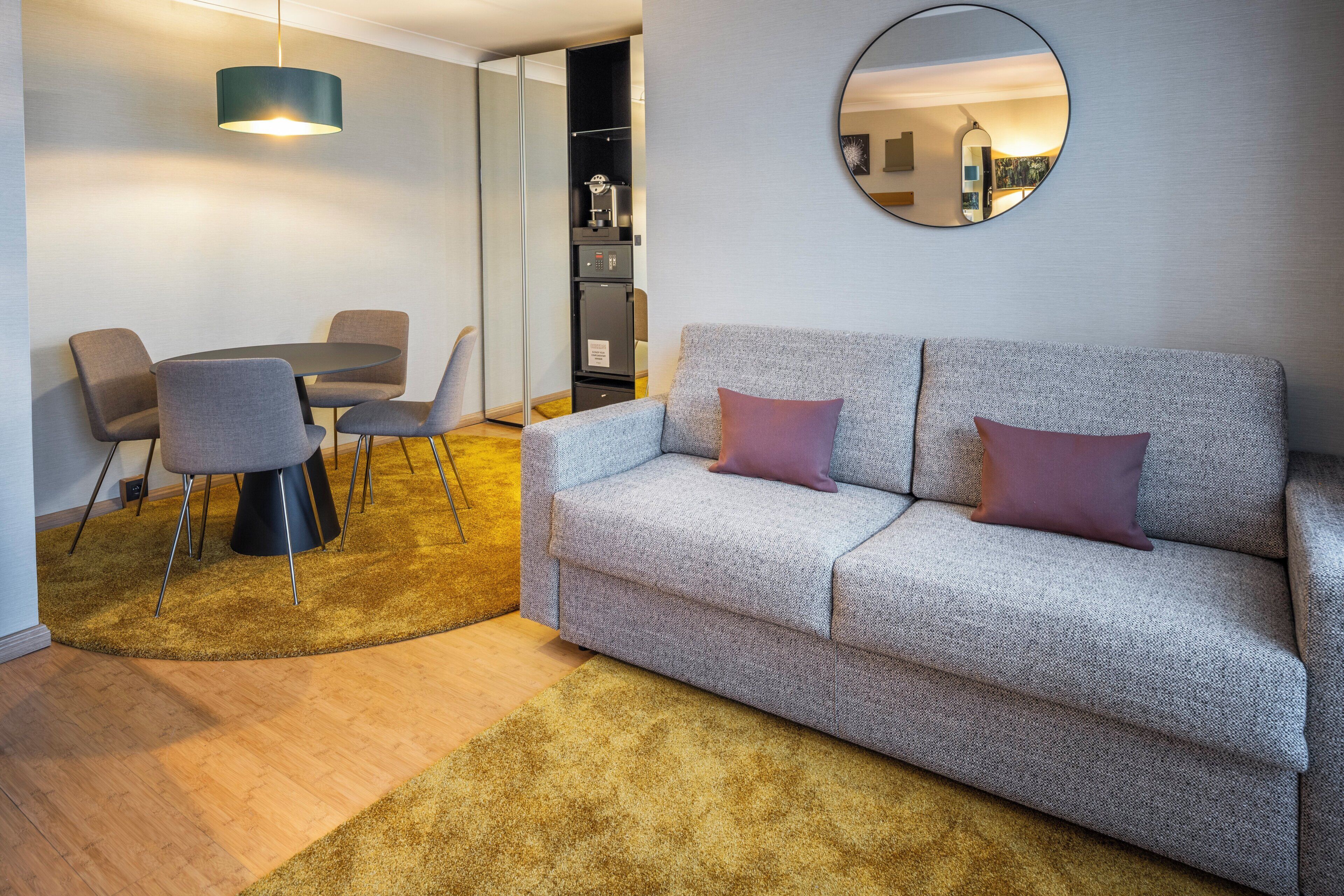 Un salon moderne comprenant un canapé, deux fauteuils, une petite table, un miroir rond et une table basse.