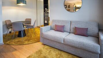A modern living room with a sofa, two chairs, a small table, a round mirror, and a coffee table.