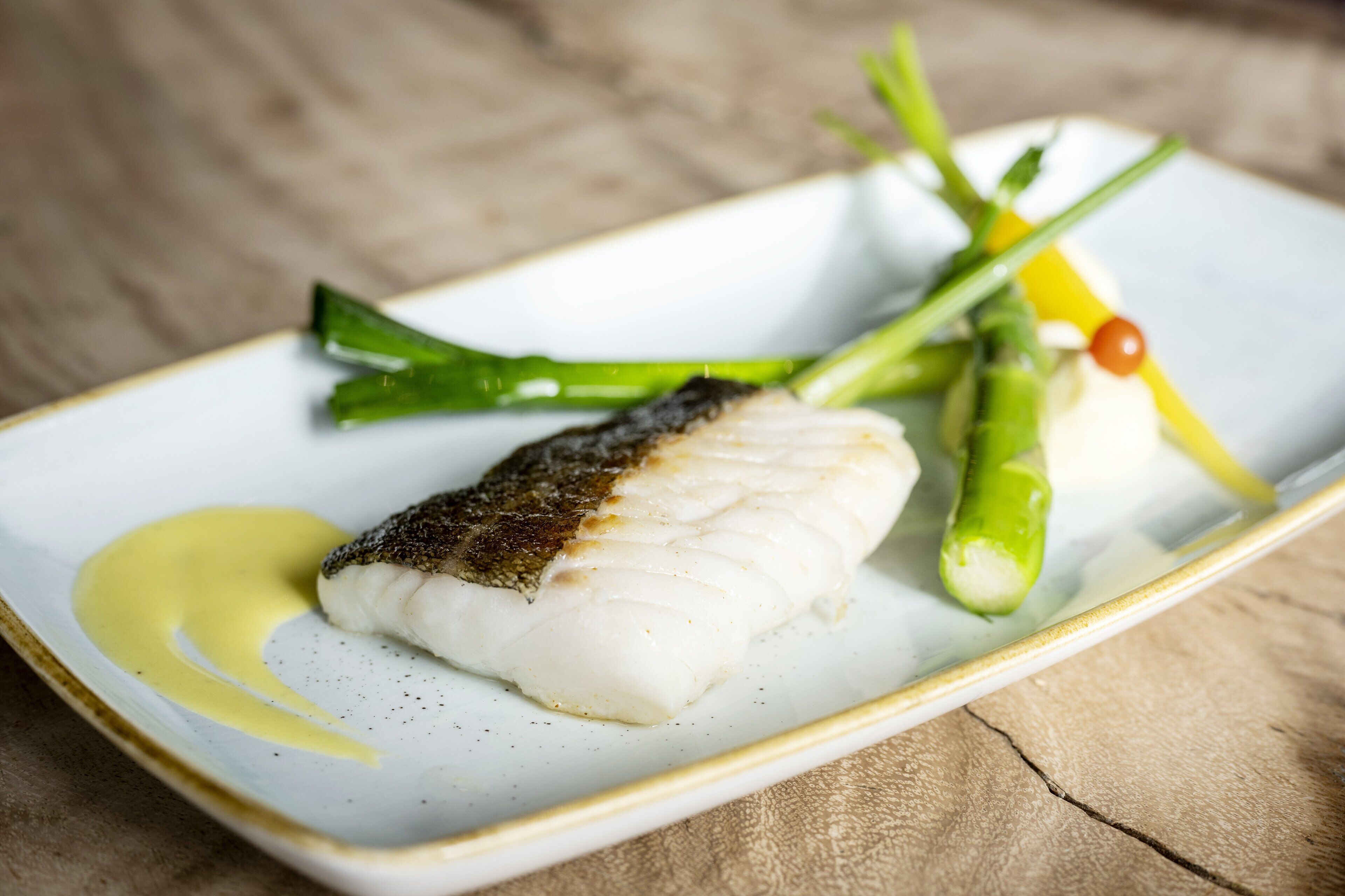 A white plate with a piece of fish, green asparagus, and a small red pepper.
