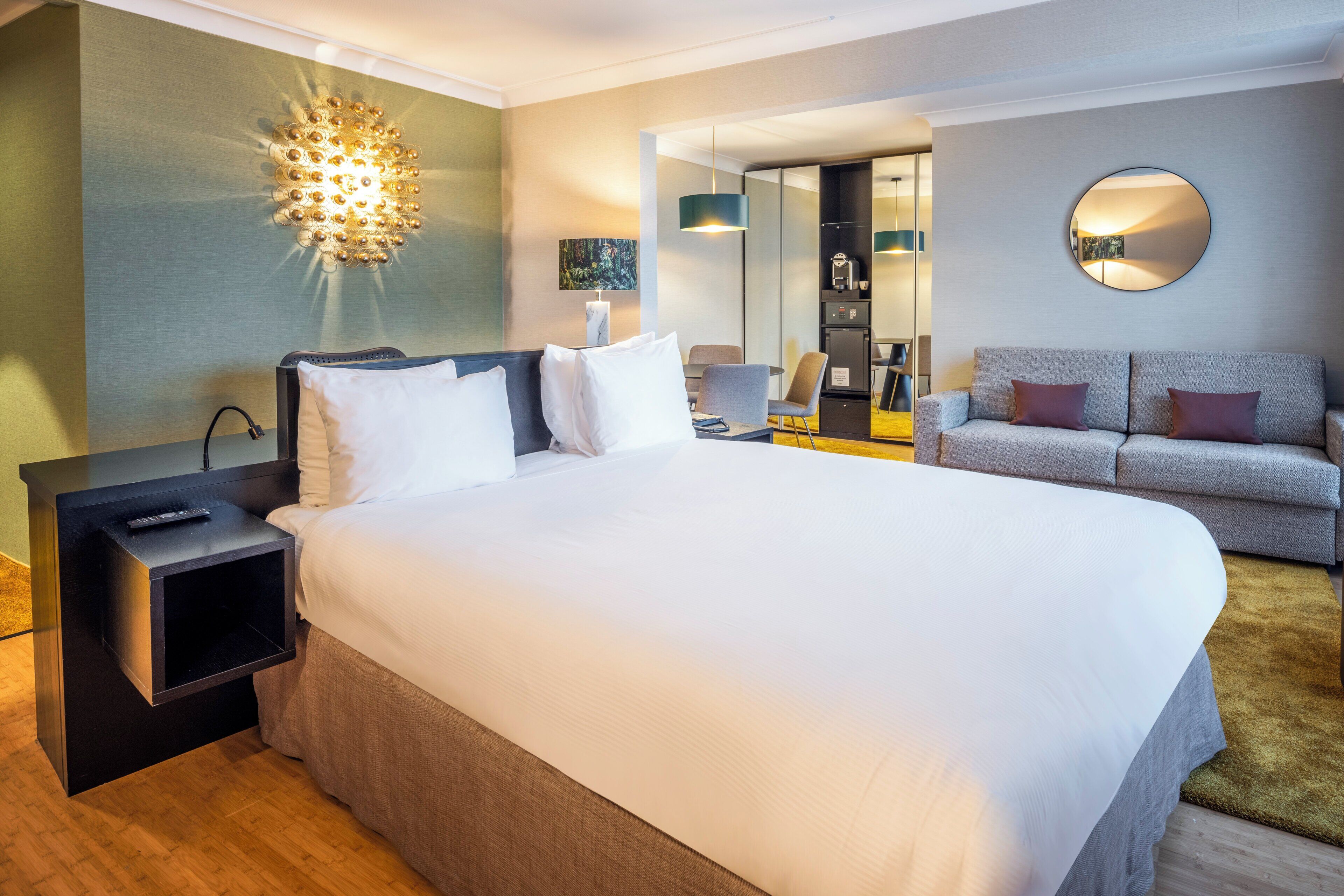 A hotel room with a large bed, bedside tables, a sofa, a desk, and a mirror.