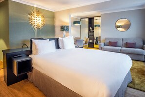 A hotel room with a large bed, bedside tables, a sofa, a desk, and a mirror.