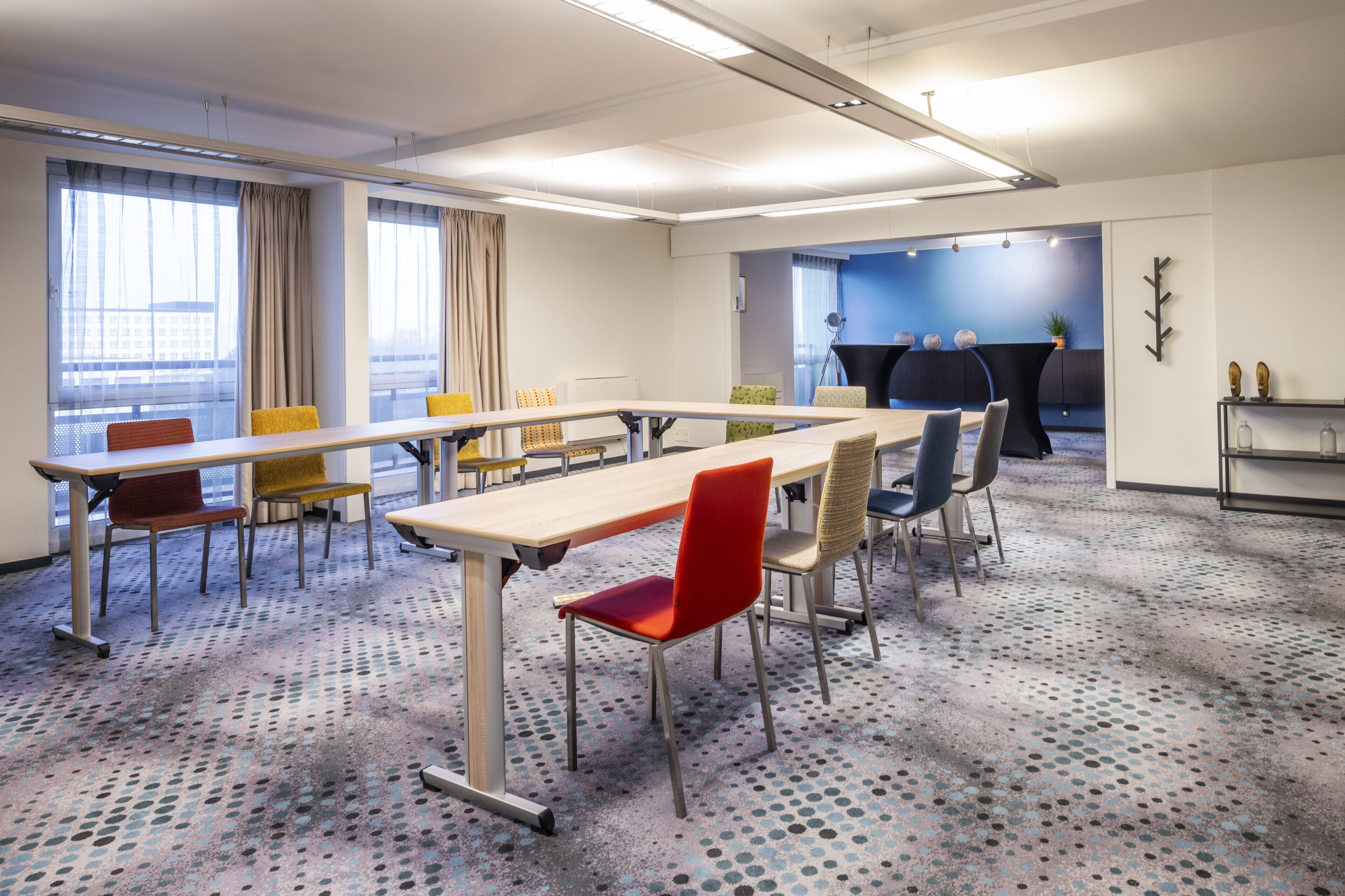 Ein Konferenzraum mit einem langen Tisch, mehreren Stühlen, einer Projektionsleinwand und einer Sitzgelegenheit mit blauer Wand.