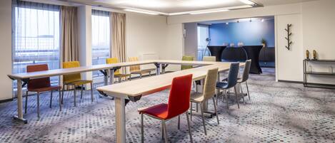 Ein Konferenzraum mit einem langen Tisch, mehreren Stühlen, einer Projektionsleinwand und einer Sitzgelegenheit mit blauer Wand.