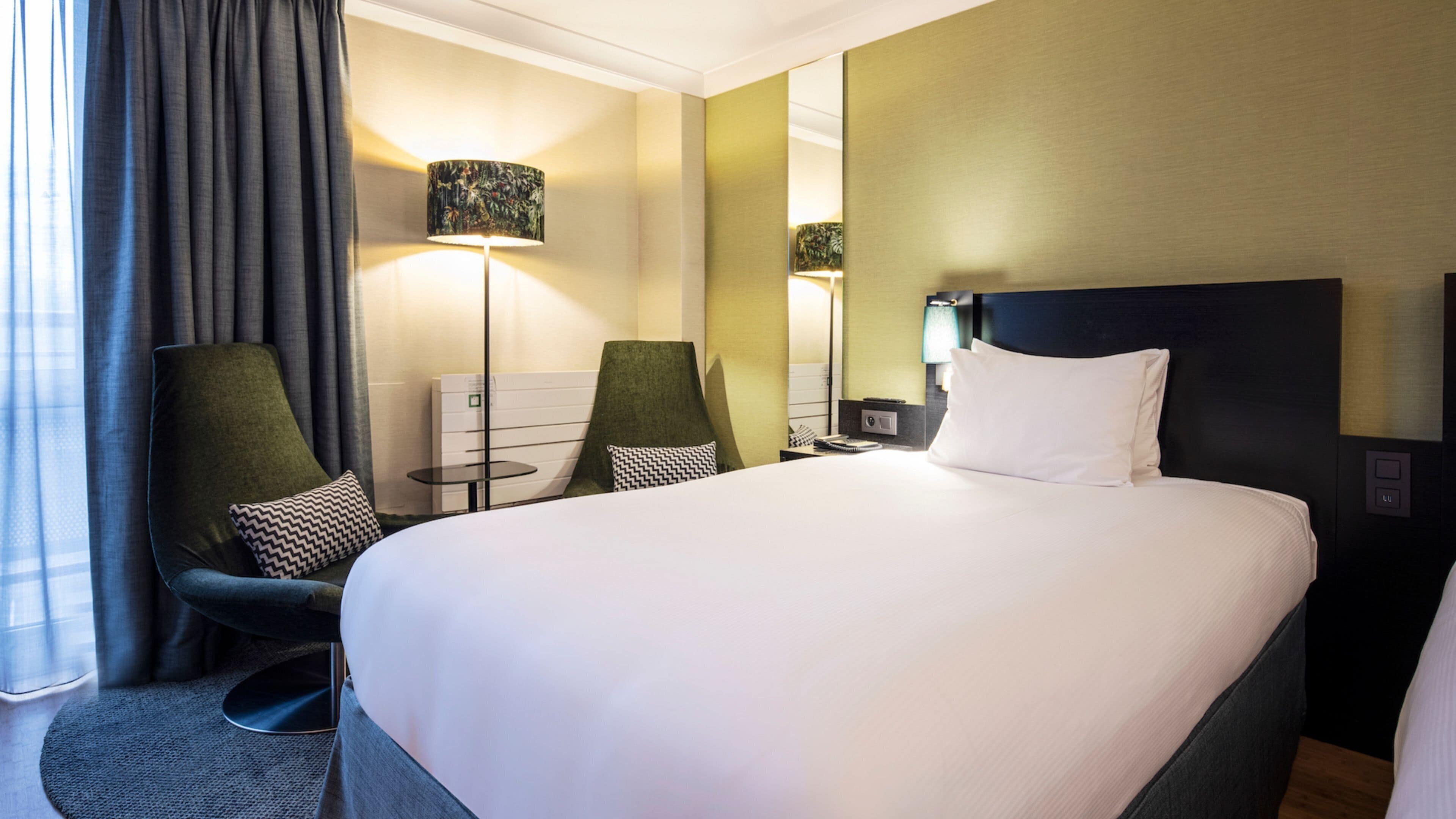 A hotel room with a large bed, two armchairs, a desk, and a lamp.