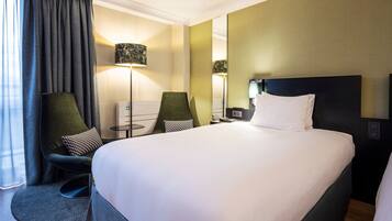 A hotel room with a large bed, two armchairs, a desk, and a lamp.