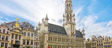 A historic building with a prominent tower and intricate architecture, surrounded by a bustling square with people and cafes.