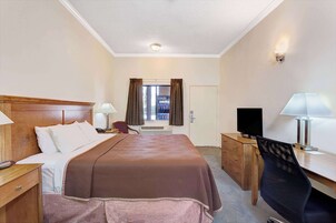 Habitación de hotel con cama, escritorio, silla, televisión y ventana con cortinas.