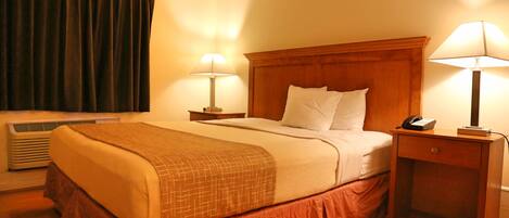 A hotel room with a large bed, two bedside lamps, a nightstand with a phone, and a window with curtains.