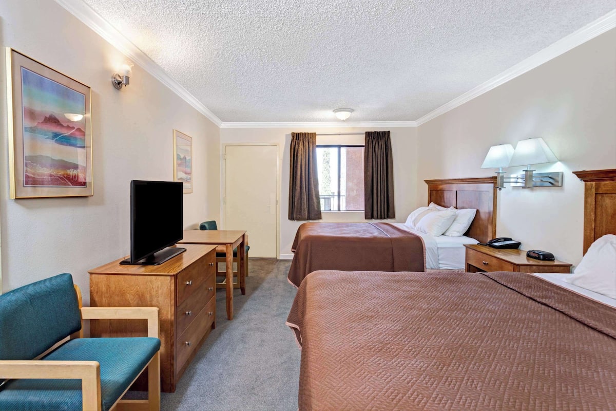 Une chambre d’hôtel avec deux lits, un bureau avec une télévision, une chaise et une commode.