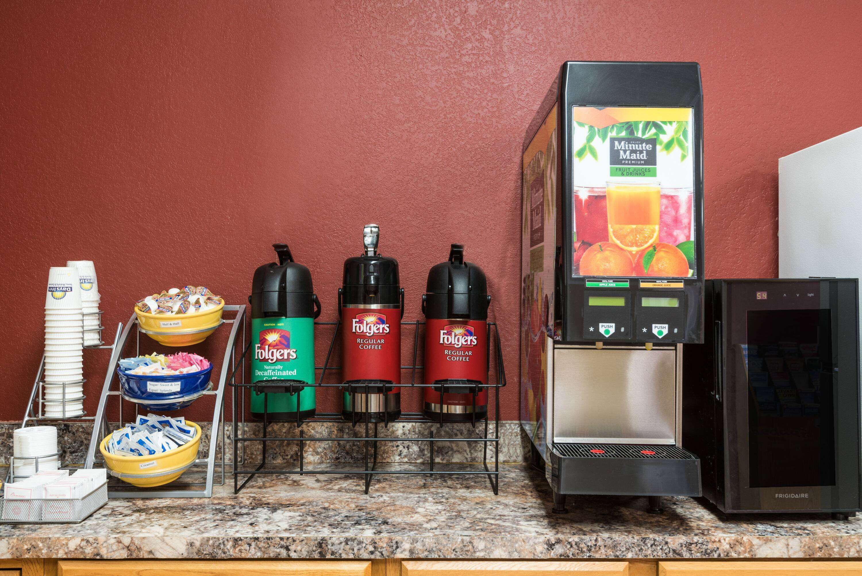 Una zona de cafè amb dosificadors de cafè Folgers, un frigorífic i un dispensador de suc.
