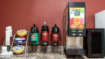 Una zona de cafè amb dosificadors de cafè Folgers, un frigorífic i un dispensador de suc.
